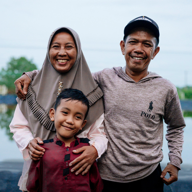 A man stands for a portrait with his wife and son at his shrimp pond in Wahyuni Mandira, Sumatra, Indonesia. 
