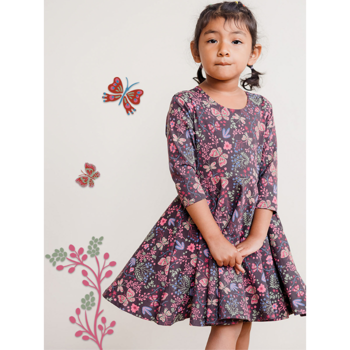 Girl standing in front of a wall with butterfly decals in a Mightly Twirl Dress
