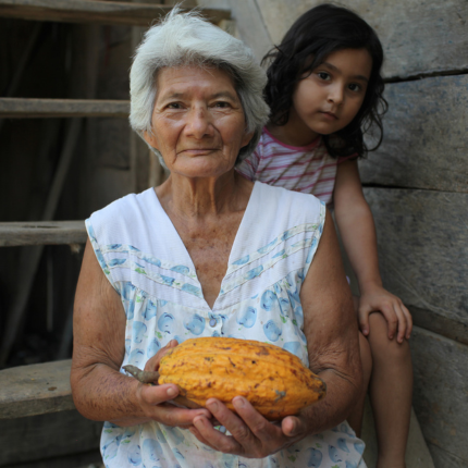 Elu Valdez, productora de cacao de toda la vida, sostiene una vaina de cacao mientras está sentada en sus escaleras con su bisnieta